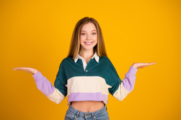 Young smiling woman in a colorful sweatshirt gesturing with open hands on a vibrant yellow...
