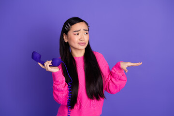 Portrait of a young Asian woman holding a purple phone expressing curiosity wearing a stylish pink...