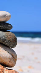A cairn of balanced stones on a sandy beach, symbolizing harmony, stability, and serenity with a tranquil ocean background.