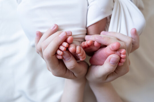 Mom and dad hands hold small legs of their two newborn twin babies