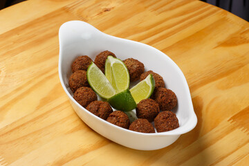 Delicious portion of fried kibbeh balls with fresh lime wedges, served in a white ceramic bowl on a wooden table.