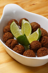 Delicious portion of fried kibbeh balls with fresh lime wedges, served in a white ceramic bowl on a wooden table.