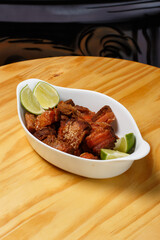 Pork rinds (torresmo), typical Brazilian food with fresh lime wedges, served in a white ceramic bowl on a wooden table.