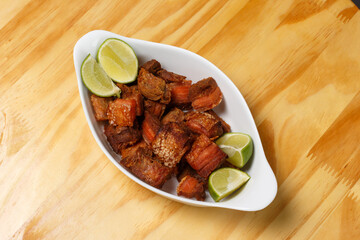 Pork rinds (torresmo), typical Brazilian food with fresh lime wedges, served in a white ceramic...
