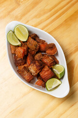 Pork rinds (torresmo), typical Brazilian food with fresh lime wedges, served in a white ceramic bowl on a wooden table.