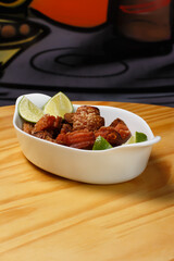 Pork rinds (torresmo), typical Brazilian food with fresh lime wedges, served in a white ceramic bowl on a wooden table.
