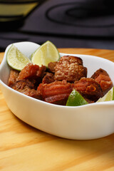 Pork rinds (torresmo), typical Brazilian food with fresh lime wedges, served in a white ceramic bowl on a wooden table.