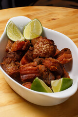 Pork rinds (torresmo), typical Brazilian food with fresh lime wedges, served in a white ceramic bowl on a wooden table.