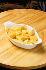 Delicious portion of fried manioc, or cassava, served in a white ceramic bowl on a wooden table.