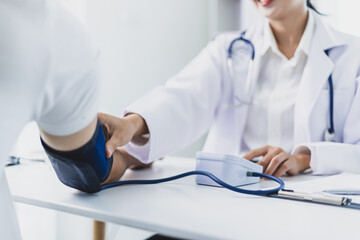 Female doctor measuring blood pressure of patient in hospital room. Doctor using sphygmomanometer...