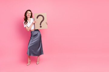 Young elegant woman holding question signboard on pink backdrop, showcasing fashion, lifestyle, and...