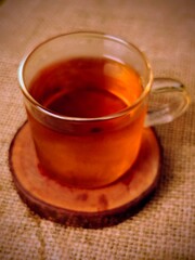 Amber Tea in Glass Cup on Rustic Wooden Coaster Burlap Background.