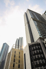 Three modern skyscrapers with glass and concrete facades rise against a partly cloudy sky, representing urban growth and architectural design.