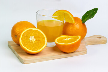 Fresh oranges and a glass of refreshing orange juice on a wooden board