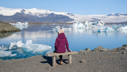 At Jokulsarlon Glacier Lagoon, a tranquil moment unfolds as a visitor sits on a wooden bench,...