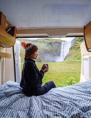A traveler sits comfortably inside a camper van, sipping a warm drink while gazing at the majestic...