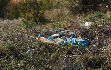 Littered area with plastic waste and debris among dry grass and shrubs