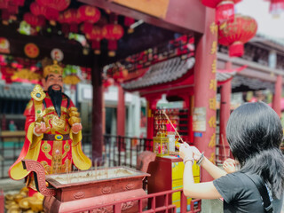 A young girl prays while holding incense in her hand as a sign of respect to the god of wealth. Visiting a religious tourist attraction.