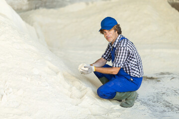 Male worker takes handful of powdered feed in palm of hand, checks purity and absence of...