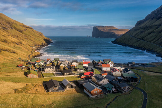 Aerial view of a quaint village nestled between steep cliffs where the ocean meets the shore with a dramatic sea stack in the distance, Tj&Atilde;&cedil;rnuv&Atilde;&shy;k, Faroe Islands.