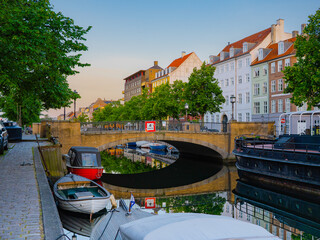 Snorrebro in Christianshavn, Copenhagen, glows at sunset with colorful buildings, boats, and a...