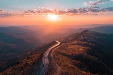 Fototapeta premium Winding road across mountaintop with vehicles during orange sunset over landscape