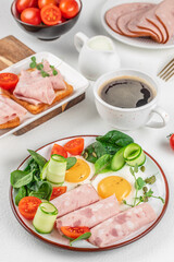 Healthy breakfast with eggs, cold cuts, fresh vegetables, and black coffee on a white background