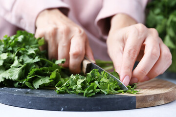 Woman cutting fresh green cilantro at light table, closeup