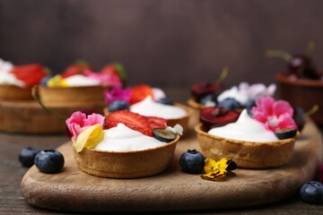 Sweet tartlets with berries and flowers on wooden table against brown background, closeup. Delicious dessert