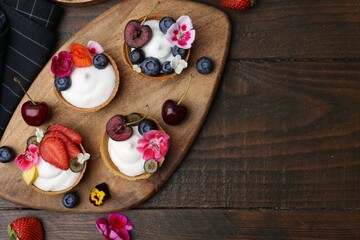 Sweet tartlets with berries and flowers on wooden table, flat lay with space for text. Delicious dessert