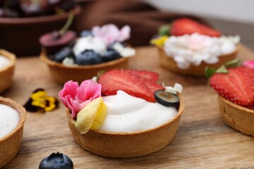 Sweet tartlets with berries and flowers on wooden board, closeup. Delicious dessert