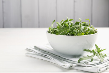 Fresh ripe green arugula leaves in bowl on white wooden table, closeup. Space for text