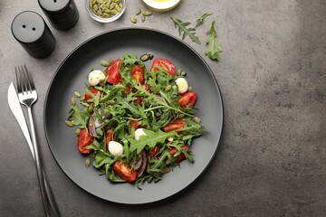 Tasty salad with arugula, mozzarella and vegetables served on grey table, flat lay. Space for text