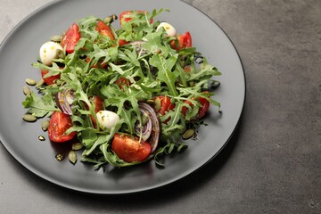 Tasty salad with arugula, mozzarella and vegetables on grey table, closeup. Space for text