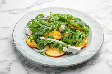 Tasty salad with arugula, cheese, peach and basil on white marble table, closeup