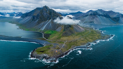 Breathtaking views of Icelands coastline reveal towering mountains shrouded in mist, lush green...