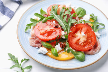 Tasty salad with arugula, cheese, tomatoes, nuts and prosciutto on white wooden table, closeup