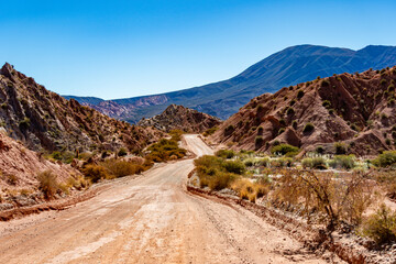 Vast and rugged desert landscape with a dusty road leading into the distant mountains of the Argentine Andes.