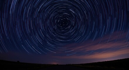 Star trails form concentric circles above a dark landscape under a night sky with some clouds