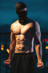 Muscular athlete with mask posing powerfully at night, showcasing strength and mystery, Toned man with face covering displaying power and intensity in evening silhouette