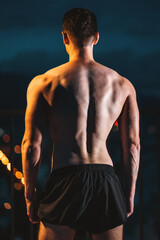 Muscular athlete with perfect physique posing from back at night, strength and dedication, Toned...