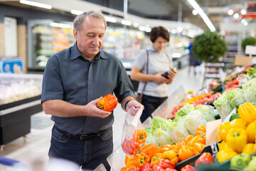 elderly man chooses pepper in vegetable and fruit department