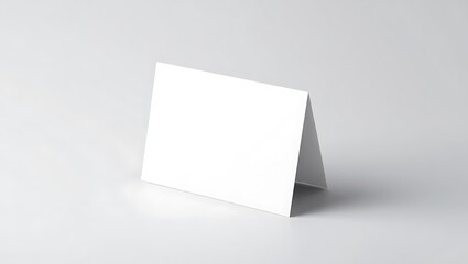 A blank white card is standing upright on a white surface against a white background in a studio