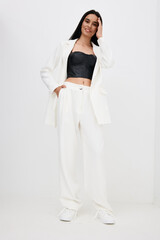 stylish woman wearing white oversized suit and black crop top standing confidently against plain white background with casual pose and natural smile