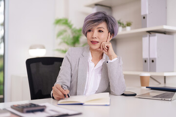 Asian adult businesswoman deep in thought planning future strategies working at modern office desk