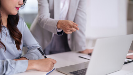 Adult Asian business professional notes strategy during office meeting with colleague guidance on laptop for corporate development and productivity