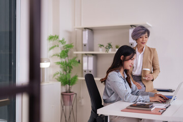 Asian business women collaborate on laptop computer in modern office environment driving...