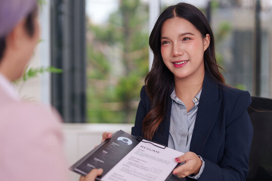 Asian adult woman applicant confidently submits resume during professional job interview recruitment process seeking new career opportunity in office setting