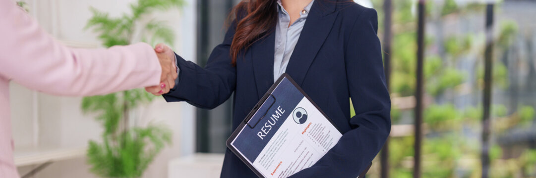 Professional adult women handshake job interview for career opportunity holding resume in modern office recruitment success