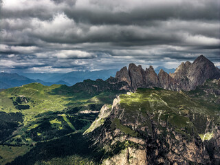 Dramatic aerial view of the Dolomites with Seceda peaks in the distance under a moody cloudy sky — South Tyrol, Italy